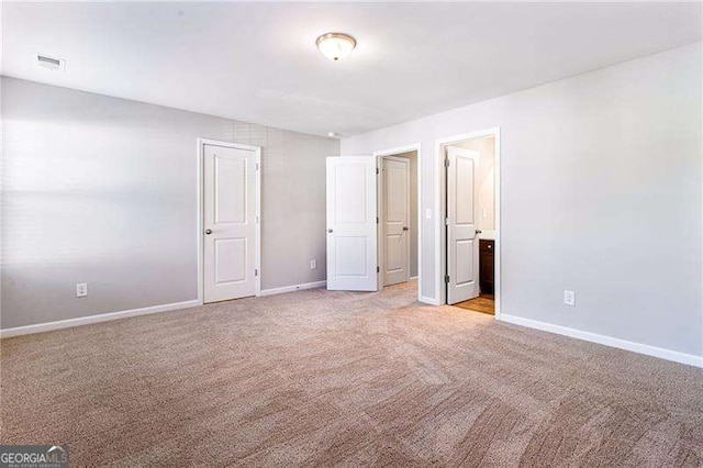 unfurnished bedroom with light carpet, ensuite bathroom, visible vents, and baseboards