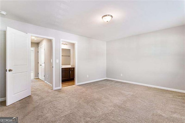 unfurnished bedroom with light colored carpet, ensuite bath, and baseboards