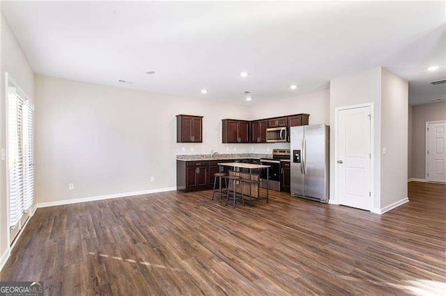 kitchen with appliances with stainless steel finishes, a kitchen breakfast bar, dark wood finished floors, and a center island