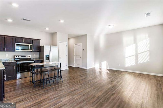 kitchen with dark brown cabinetry, visible vents, appliances with stainless steel finishes, a breakfast bar area, and dark wood-type flooring