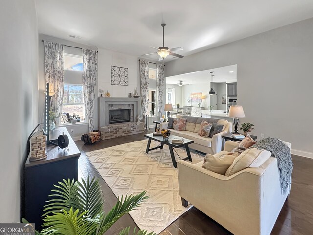 living room featuring visible vents, dark wood-type flooring, baseboards, ceiling fan, and a fireplace