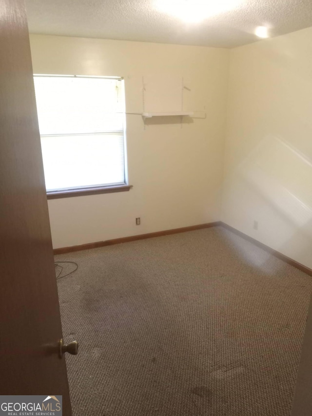 empty room featuring a textured ceiling, carpet flooring, and baseboards