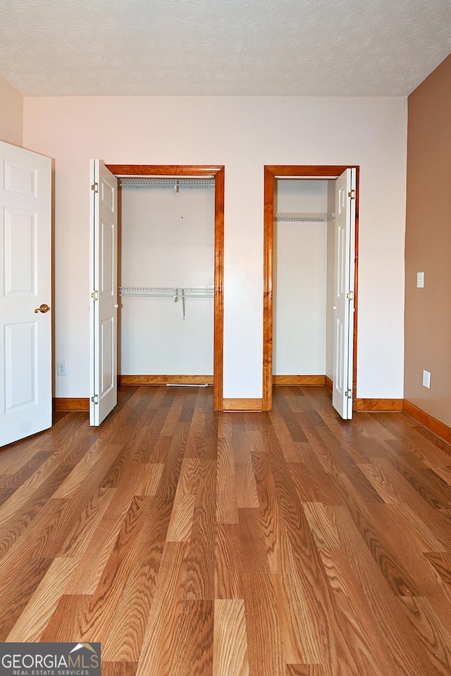 unfurnished bedroom featuring a textured ceiling, multiple closets, wood finished floors, and baseboards