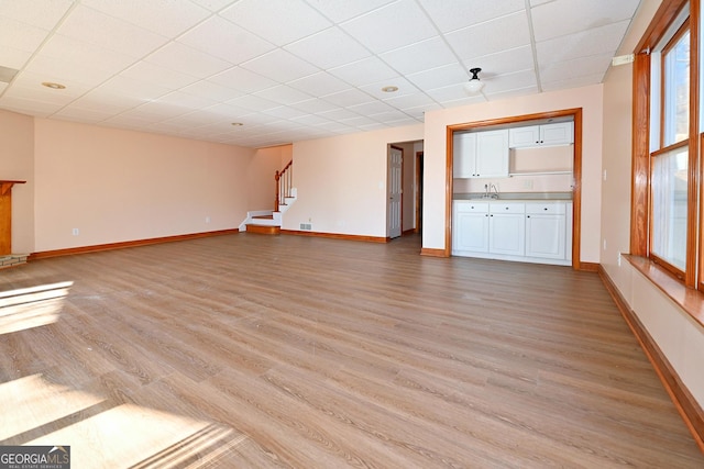 unfurnished living room with light wood-style flooring, stairs, baseboards, and a sink