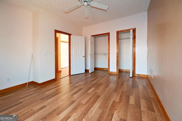 unfurnished bedroom featuring a textured ceiling, wood finished floors, visible vents, multiple closets, and baseboards