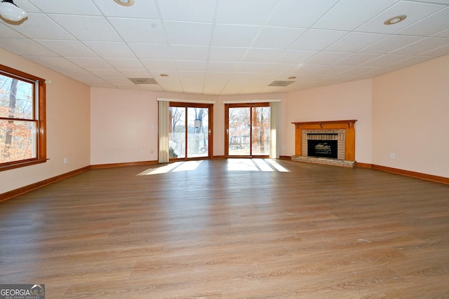 unfurnished living room with baseboards, light wood-type flooring, a paneled ceiling, and a brick fireplace