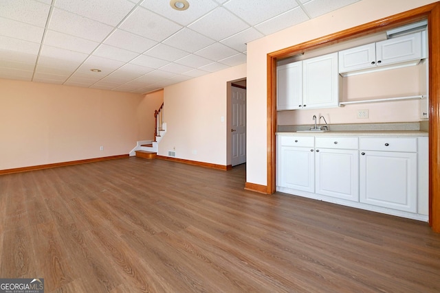 interior space featuring a paneled ceiling, a sink, baseboards, stairs, and dark wood-style floors