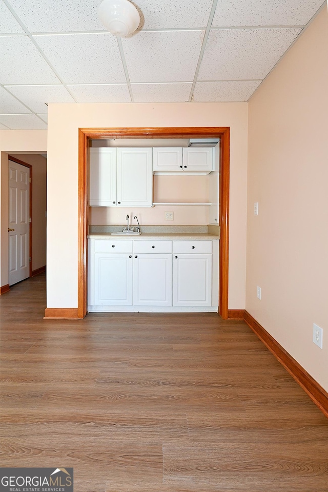 interior space with light wood finished floors, a drop ceiling, white cabinets, and baseboards