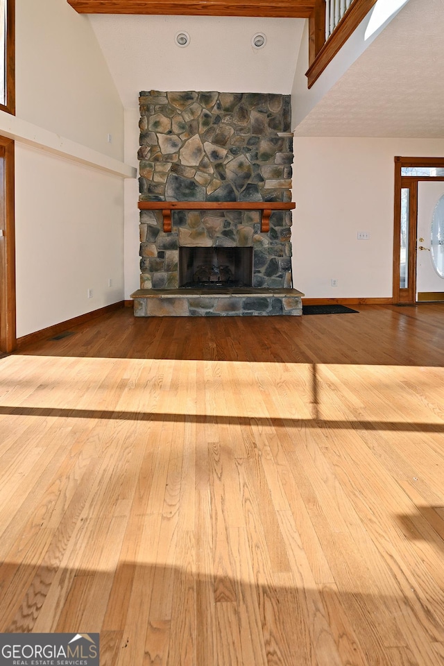 unfurnished living room with high vaulted ceiling, baseboards, a fireplace, and hardwood / wood-style floors