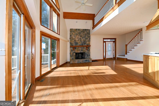 unfurnished living room with light wood finished floors, visible vents, stairway, a high ceiling, and a fireplace