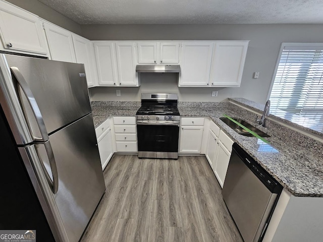 kitchen with a textured ceiling, under cabinet range hood, a sink, white cabinets, and appliances with stainless steel finishes