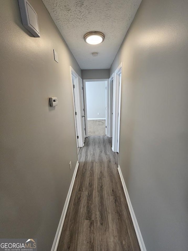 hallway featuring dark wood-style floors, baseboards, and a textured ceiling