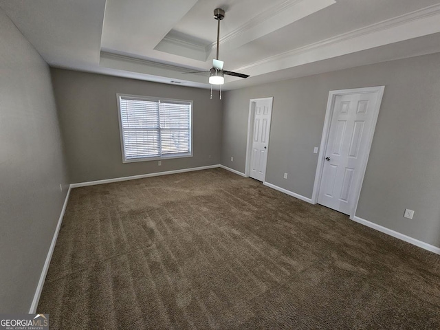 unfurnished bedroom featuring a tray ceiling, crown molding, dark colored carpet, ceiling fan, and baseboards