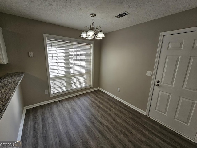 unfurnished dining area featuring visible vents, dark wood-type flooring, a textured ceiling, a chandelier, and baseboards