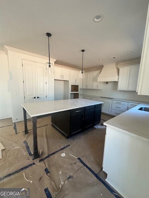 kitchen with custom range hood, a kitchen island, decorative light fixtures, light countertops, and stovetop