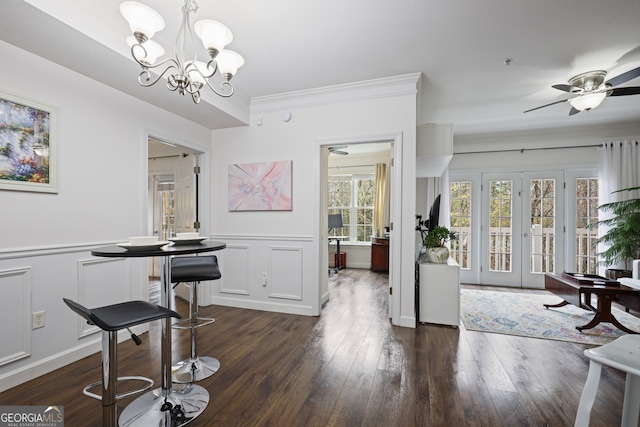 dining space featuring dark wood-style floors, a wainscoted wall, ornamental molding, a decorative wall, and ceiling fan with notable chandelier