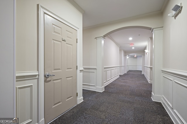 corridor featuring ornamental molding, a decorative wall, and dark colored carpet