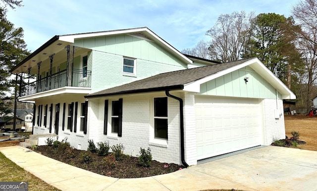 view of side of property with a shingled roof, a balcony, an attached garage, board and batten siding, and brick siding