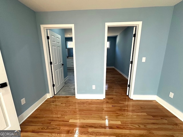 unfurnished bedroom with wood finished floors, connected bathroom, and baseboards