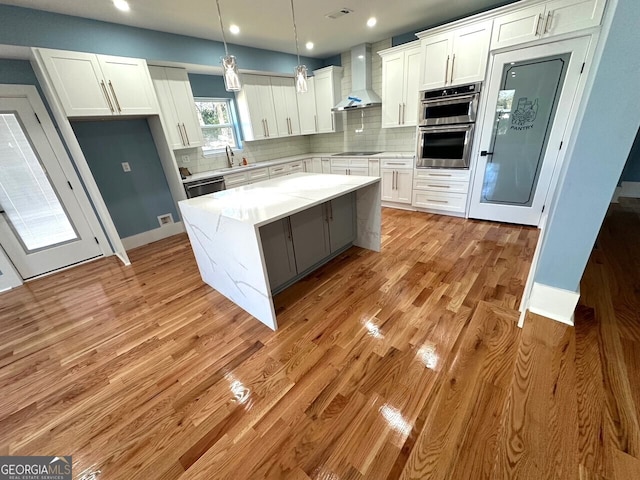 kitchen with light stone counters, white cabinets, wall chimney range hood, a center island, and pendant lighting