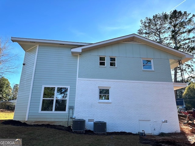 view of property exterior with board and batten siding, crawl space, brick siding, and central AC unit