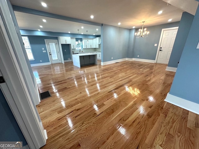 unfurnished living room featuring recessed lighting, visible vents, a chandelier, light wood-type flooring, and baseboards