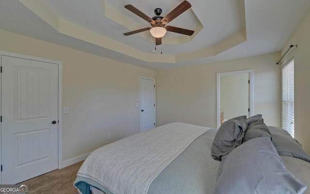 bedroom with light carpet, baseboards, a raised ceiling, and a ceiling fan