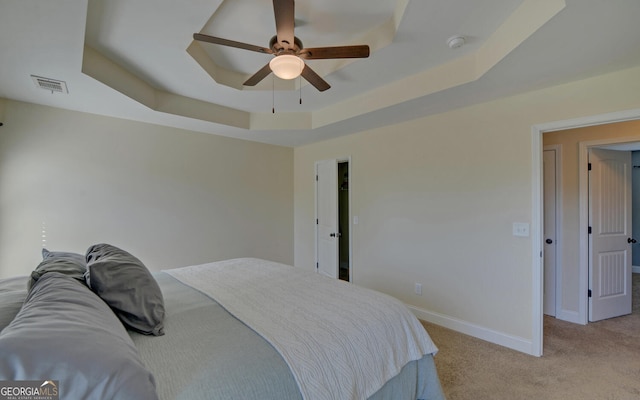 bedroom with light carpet, baseboards, visible vents, ceiling fan, and a tray ceiling