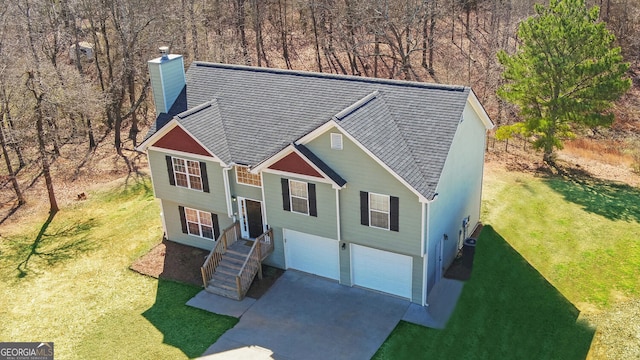 split foyer home featuring roof with shingles, driveway, a chimney, and an attached garage