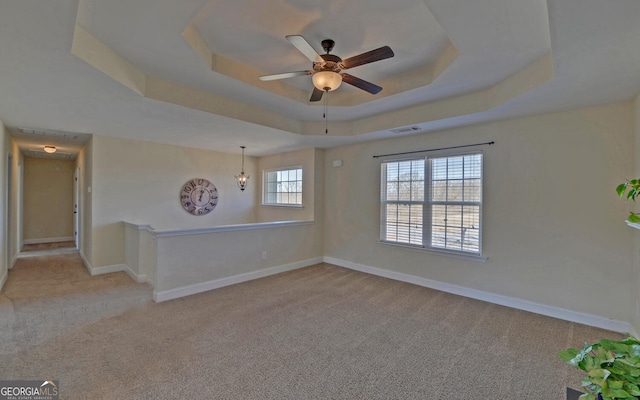 spare room with visible vents, baseboards, a raised ceiling, a ceiling fan, and light colored carpet