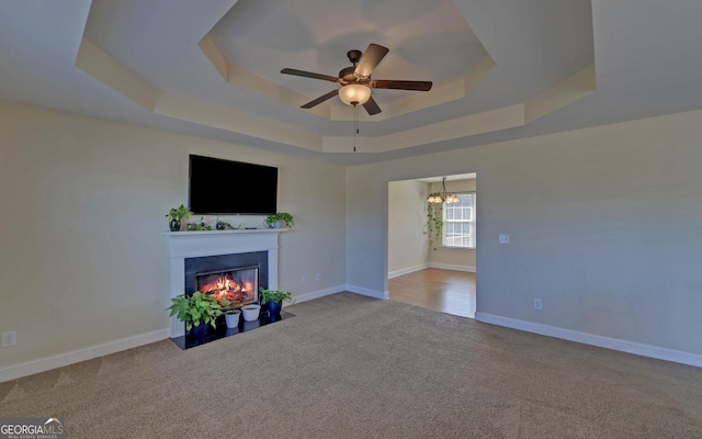 unfurnished living room featuring a tray ceiling, carpet flooring, a fireplace with flush hearth, and baseboards