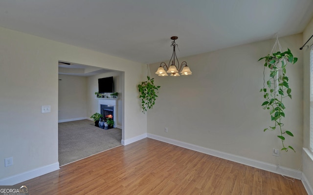 unfurnished room featuring light wood-type flooring, a warm lit fireplace, baseboards, and an inviting chandelier