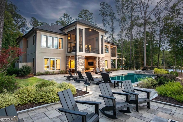 back of property with stone siding, a sunroom, a patio area, and a fireplace