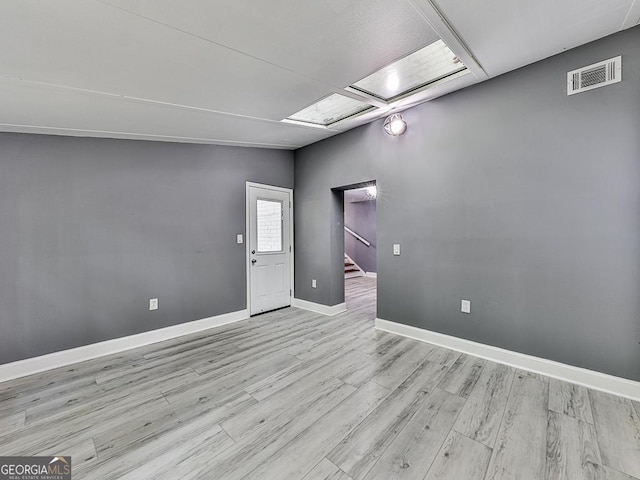 empty room with stairs, light wood finished floors, visible vents, and baseboards