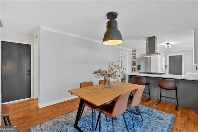 dining space with ornamental molding, light wood-style flooring, and baseboards