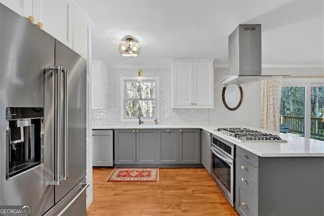 kitchen with island exhaust hood, stainless steel appliances, light countertops, gray cabinetry, and a sink