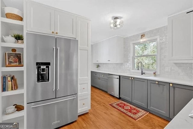 kitchen featuring appliances with stainless steel finishes, gray cabinets, light countertops, open shelves, and a sink