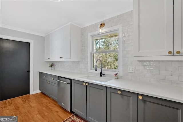 kitchen featuring gray cabinets, crown molding, light countertops, stainless steel dishwasher, and backsplash