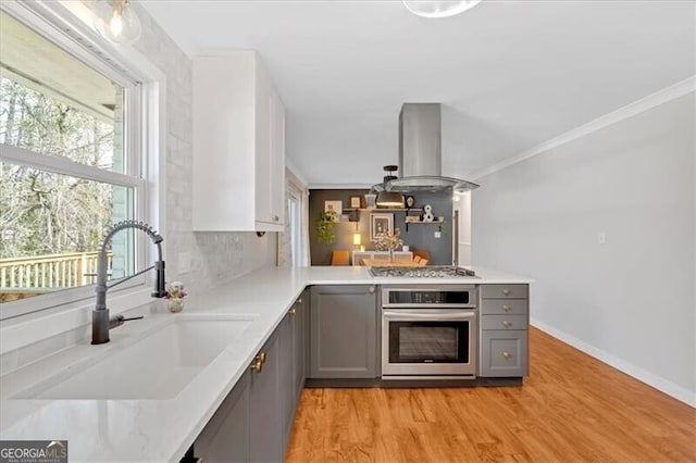 kitchen with island exhaust hood, light countertops, appliances with stainless steel finishes, a sink, and a peninsula