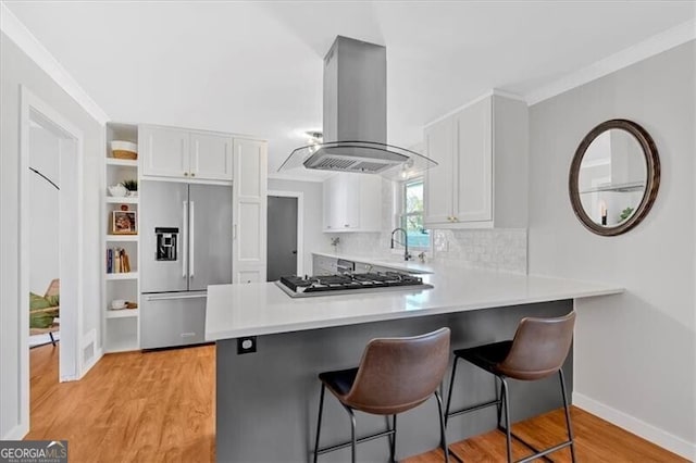 kitchen with island exhaust hood, stainless steel appliances, light countertops, white cabinets, and a peninsula