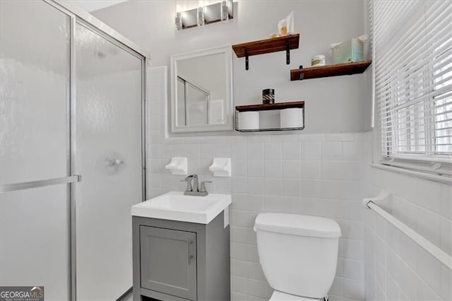 full bath featuring a wainscoted wall, a shower with door, tile walls, toilet, and vanity