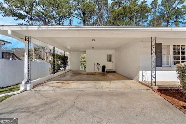 view of vehicle parking featuring driveway, a carport, and fence