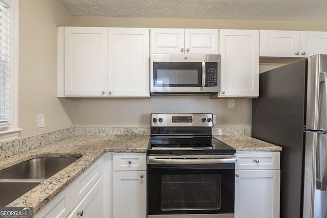 kitchen featuring white cabinets, appliances with stainless steel finishes, light stone countertops, a textured ceiling, and a sink