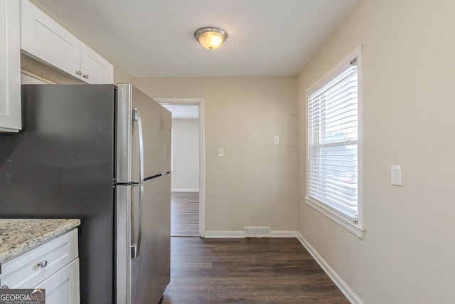 kitchen with plenty of natural light, visible vents, white cabinets, freestanding refrigerator, and light stone countertops