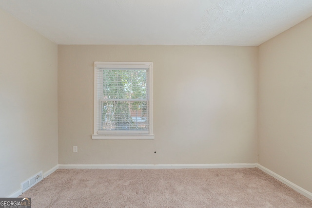 unfurnished room with light carpet, a textured ceiling, visible vents, and baseboards