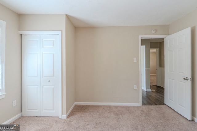 unfurnished bedroom featuring baseboards, a closet, and light colored carpet