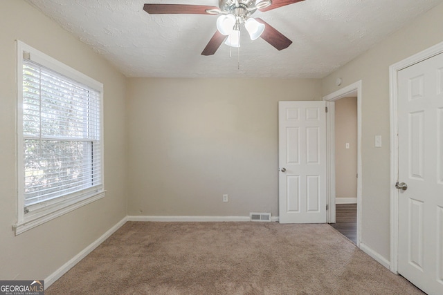 spare room with carpet floors, visible vents, a textured ceiling, and baseboards