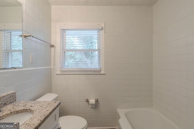 full bathroom with a tub to relax in, toilet, a textured ceiling, vanity, and tile walls