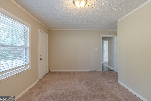 spare room featuring a textured ceiling, light carpet, visible vents, baseboards, and crown molding