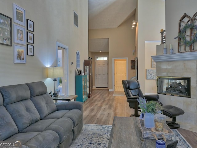 living room with a towering ceiling, light wood finished floors, a fireplace, and visible vents